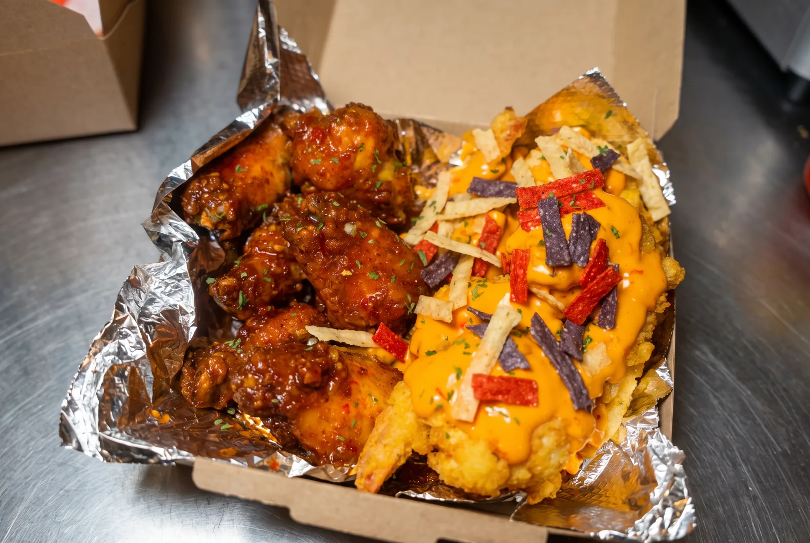 Dah's Kitchen sauced jumbo wings and loaded cheese fries in a takeout box